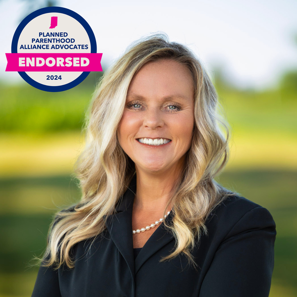 Blonde woman in a suit jacket stands in front of a green field. There is a PPAA endorsement badge.